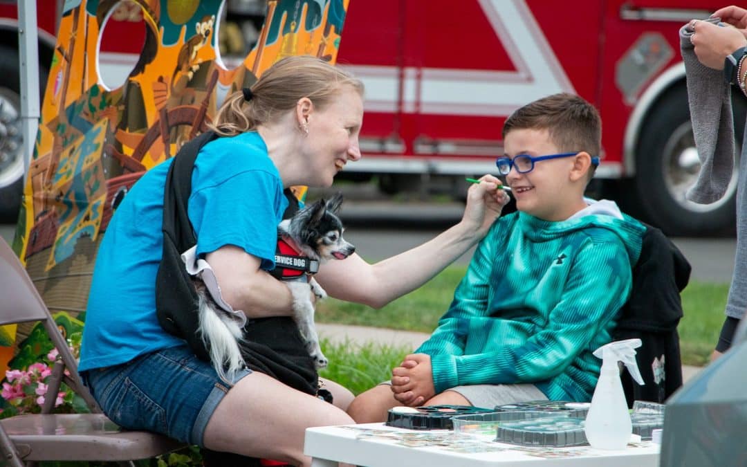 A boy gets his face painted by a member of the Enfield Youth Council, accompanied by a service dog.